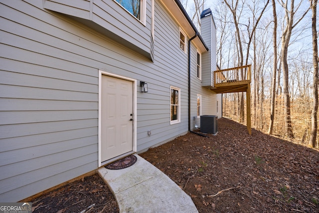 view of exterior entry featuring central air condition unit and a chimney