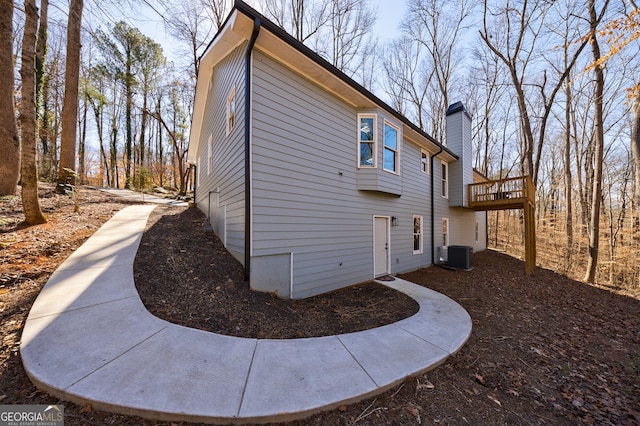 view of home's exterior featuring a chimney, a wooden deck, and central AC unit