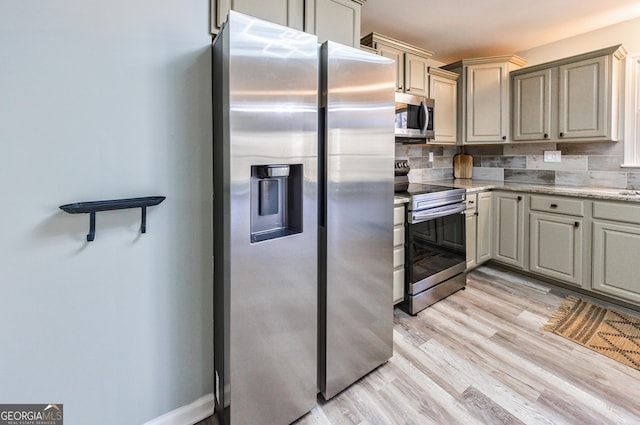 kitchen featuring appliances with stainless steel finishes, light stone countertops, light wood finished floors, and tasteful backsplash