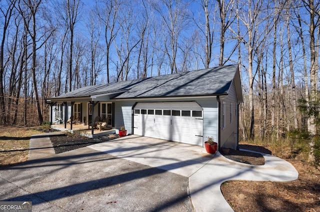 view of side of home featuring covered porch, driveway, roof with shingles, and a garage