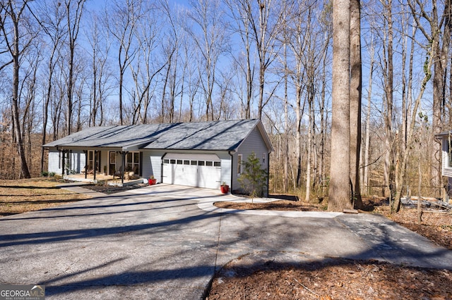 view of side of home featuring covered porch, driveway, roof with shingles, and an attached garage