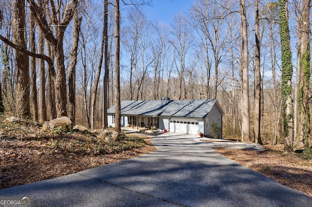 view of front of home featuring aphalt driveway, a view of trees, and an attached garage