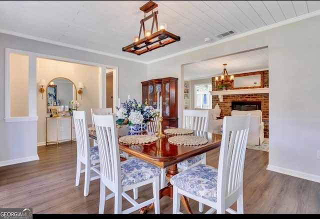 dining space featuring a brick fireplace, a chandelier, dark wood-type flooring, and ornamental molding