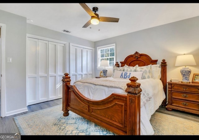 bedroom featuring hardwood / wood-style flooring, two closets, and ceiling fan