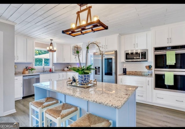 kitchen featuring appliances with stainless steel finishes, white cabinets, a center island, and decorative light fixtures