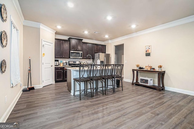 kitchen featuring a breakfast bar, stainless steel appliances, dark wood-type flooring, an island with sink, and dark brown cabinetry