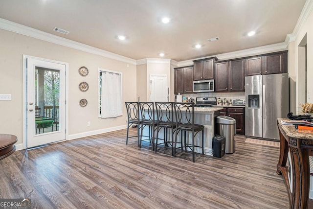 kitchen with appliances with stainless steel finishes, a kitchen island with sink, a kitchen breakfast bar, and dark brown cabinets