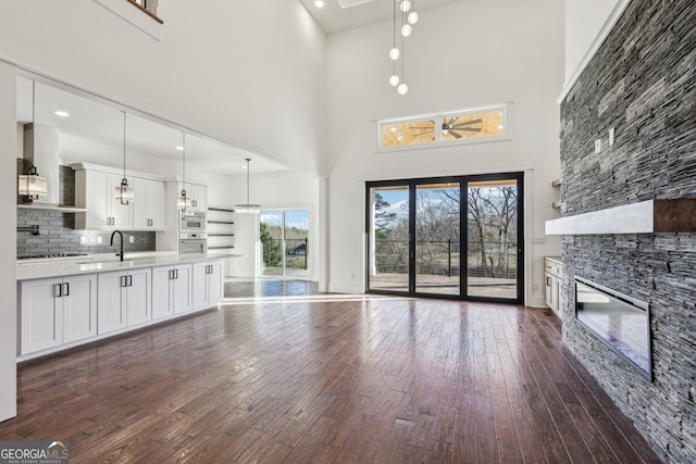 unfurnished living room featuring a stone fireplace, a high ceiling, and dark wood-type flooring