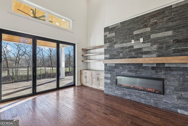 unfurnished living room featuring a fireplace, a towering ceiling, and dark hardwood / wood-style flooring