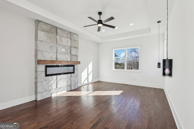 unfurnished living room featuring ceiling fan, a raised ceiling, wood-type flooring, and a tiled fireplace