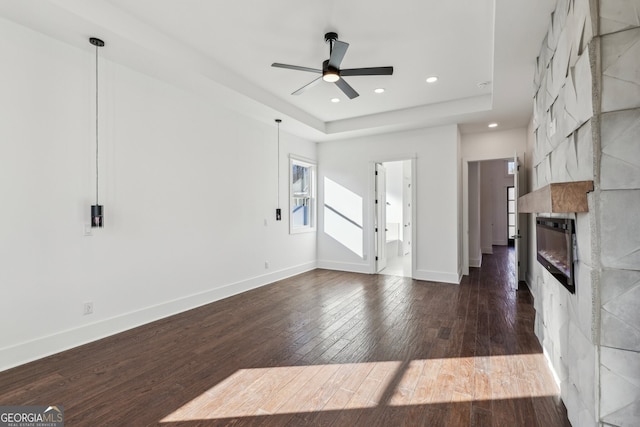 unfurnished living room featuring a fireplace, dark wood-type flooring, ceiling fan, and a tray ceiling