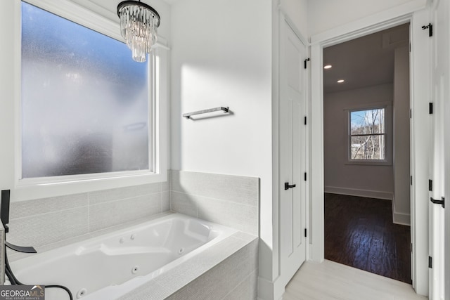 bathroom featuring tiled bath, a chandelier, and wood-type flooring