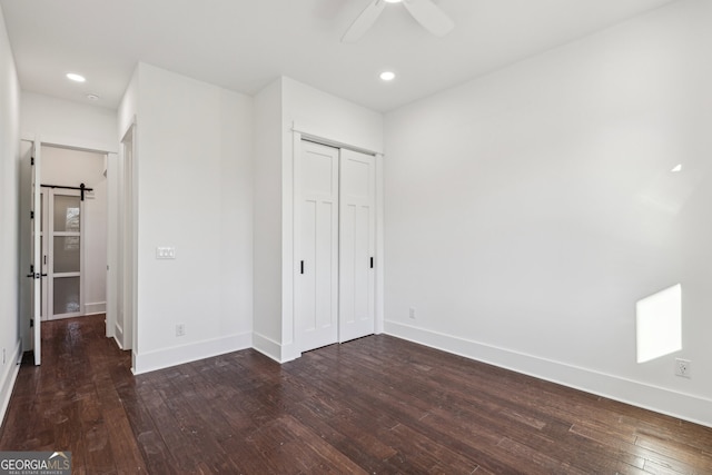 unfurnished bedroom with ceiling fan, a closet, dark hardwood / wood-style flooring, and a barn door