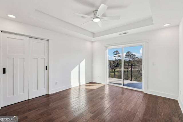 unfurnished bedroom featuring a tray ceiling, ceiling fan, dark hardwood / wood-style flooring, and access to exterior