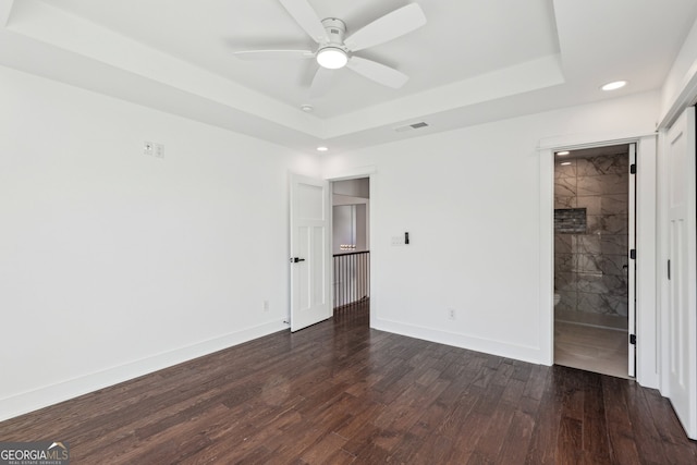 unfurnished bedroom with a tray ceiling, ensuite bath, and dark hardwood / wood-style floors