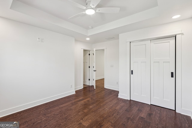 unfurnished bedroom featuring dark hardwood / wood-style flooring, ceiling fan, a raised ceiling, and a closet