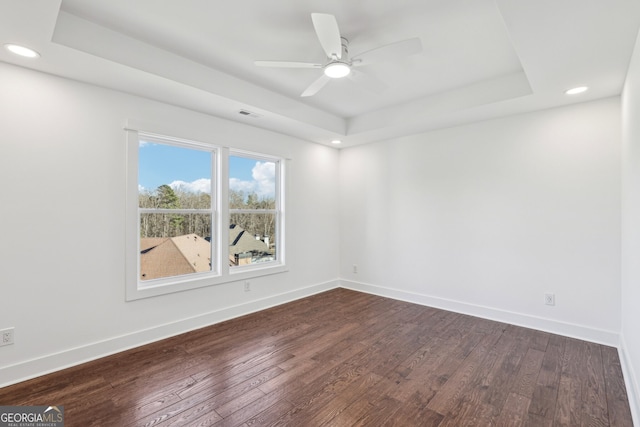 unfurnished room with a tray ceiling, ceiling fan, and dark wood-type flooring