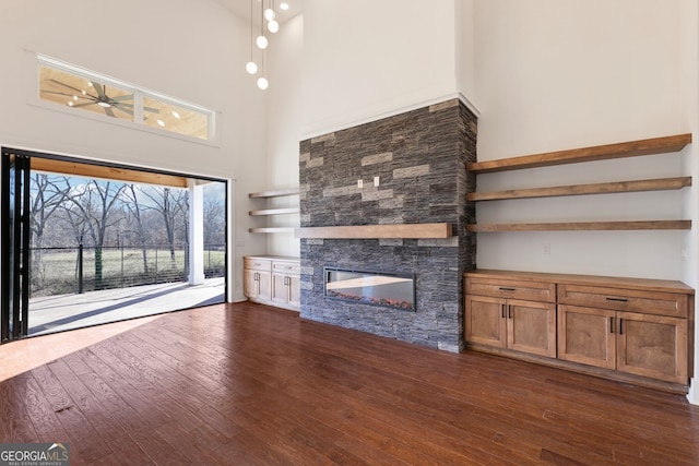 unfurnished living room featuring dark hardwood / wood-style flooring, a stone fireplace, and a high ceiling