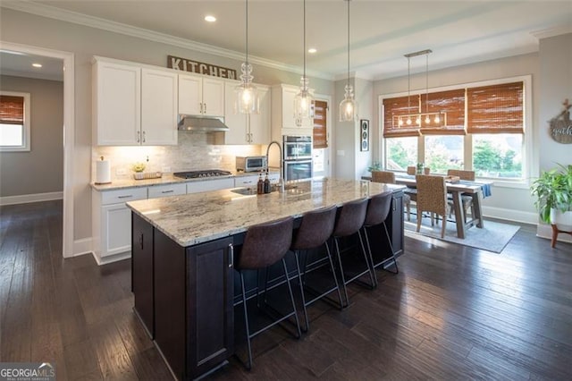 kitchen with a kitchen island with sink, hanging light fixtures, white cabinetry, and under cabinet range hood