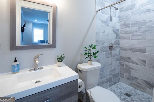 bathroom with a tile shower, vanity, and toilet