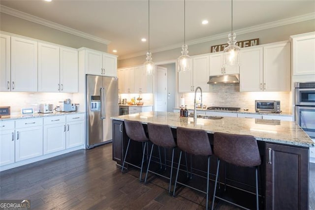 kitchen with an island with sink, appliances with stainless steel finishes, hanging light fixtures, under cabinet range hood, and white cabinetry