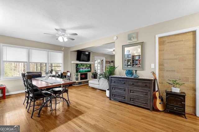 dining room featuring a textured ceiling, a wood stove, ceiling fan, and light hardwood / wood-style flooring