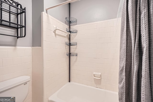 full bathroom with toilet, shower / tub combo, tile walls, and a wainscoted wall