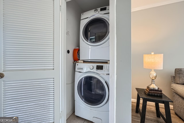 clothes washing area featuring stacked washer / drying machine, laundry area, baseboards, and light wood finished floors