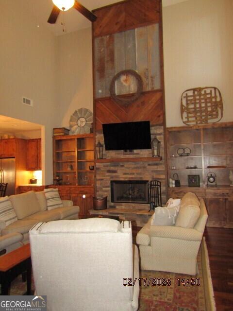 living room with hardwood / wood-style flooring, ceiling fan, a large fireplace, and a towering ceiling