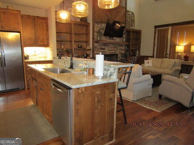 kitchen with hardwood / wood-style flooring, decorative light fixtures, stainless steel appliances, and a kitchen island with sink