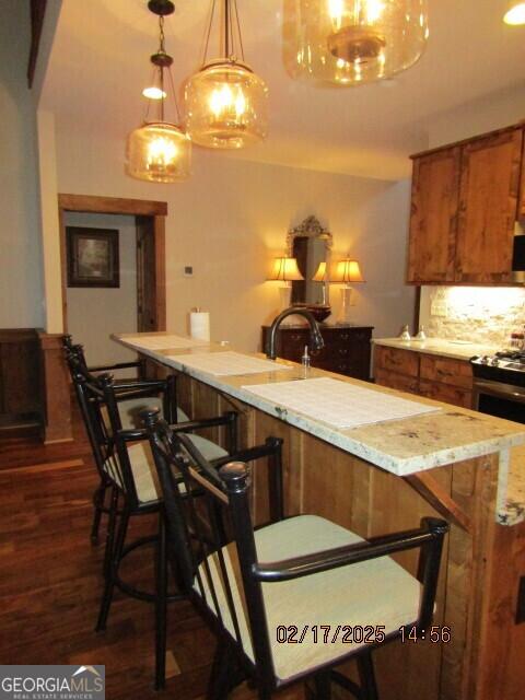 kitchen with dark hardwood / wood-style floors, decorative light fixtures, electric range, backsplash, and a kitchen bar