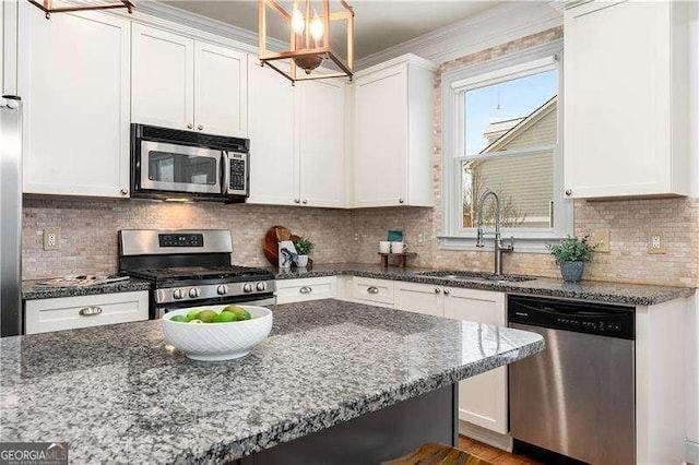 kitchen with dark stone countertops, hanging light fixtures, sink, appliances with stainless steel finishes, and white cabinets