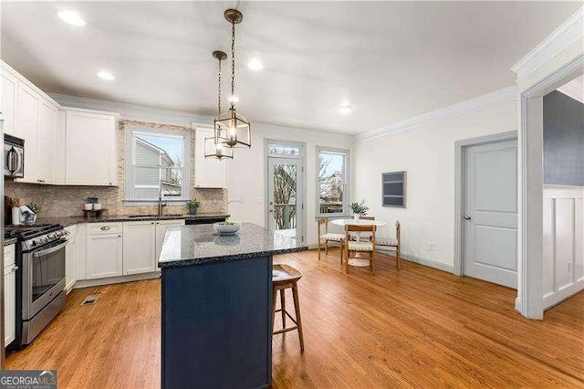 kitchen featuring appliances with stainless steel finishes, light hardwood / wood-style flooring, white cabinetry, pendant lighting, and a kitchen island