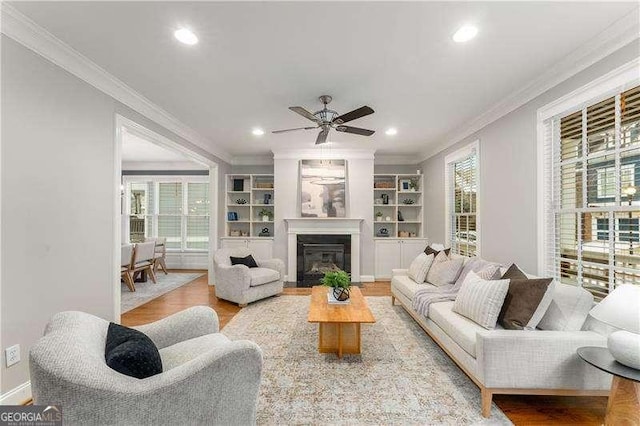 living room featuring ceiling fan, built in shelves, crown molding, and wood-type flooring