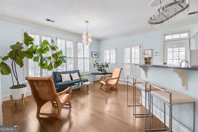 living area featuring hardwood / wood-style floors, a healthy amount of sunlight, crown molding, and a notable chandelier