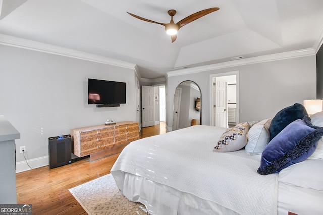 bedroom with wood-type flooring, ceiling fan, ensuite bathroom, a tray ceiling, and ornamental molding