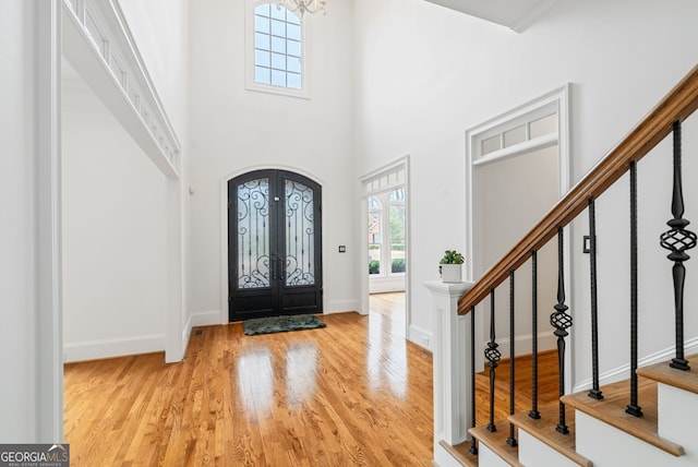 foyer entrance with an inviting chandelier, light wood-type flooring, french doors, and a towering ceiling