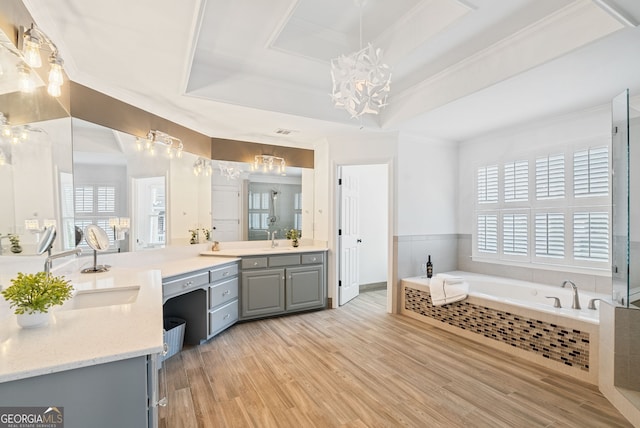 bathroom with vanity, tiled tub, a tray ceiling, crown molding, and hardwood / wood-style flooring