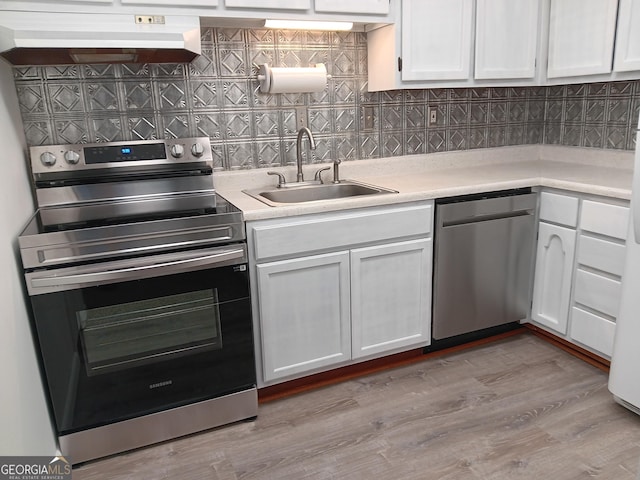 kitchen featuring appliances with stainless steel finishes, a sink, under cabinet range hood, backsplash, and light countertops