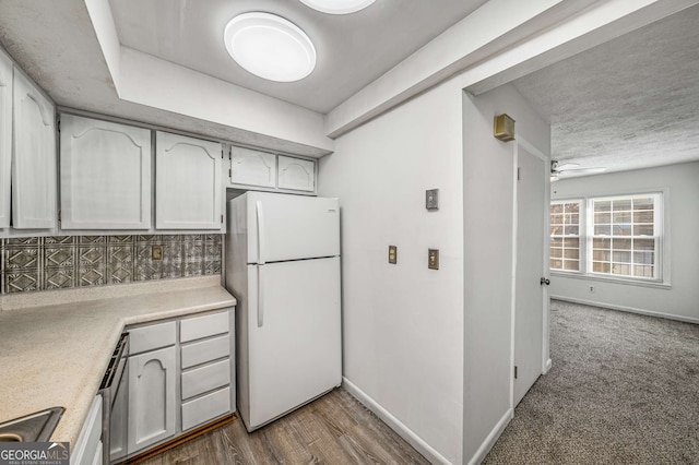 kitchen featuring freestanding refrigerator, light countertops, decorative backsplash, ceiling fan, and baseboards
