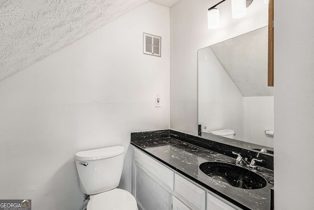 half bathroom with toilet, lofted ceiling, a textured ceiling, and vanity