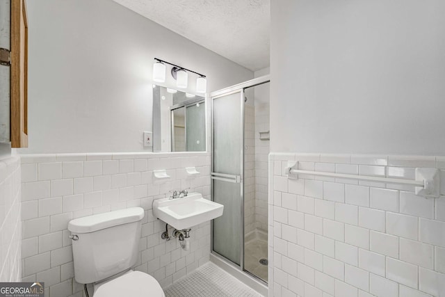 full bathroom featuring tile walls, a stall shower, wainscoting, toilet, and a sink