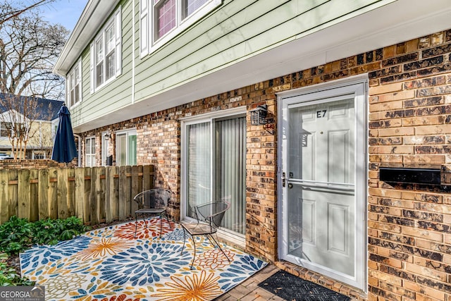 view of exterior entry featuring brick siding and fence