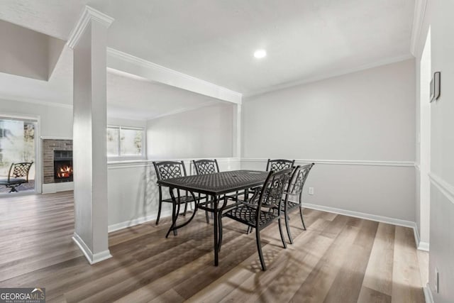 dining space with a brick fireplace, crown molding, and wood-type flooring