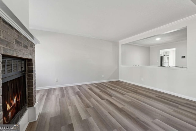 unfurnished living room with a brick fireplace, crown molding, and wood-type flooring