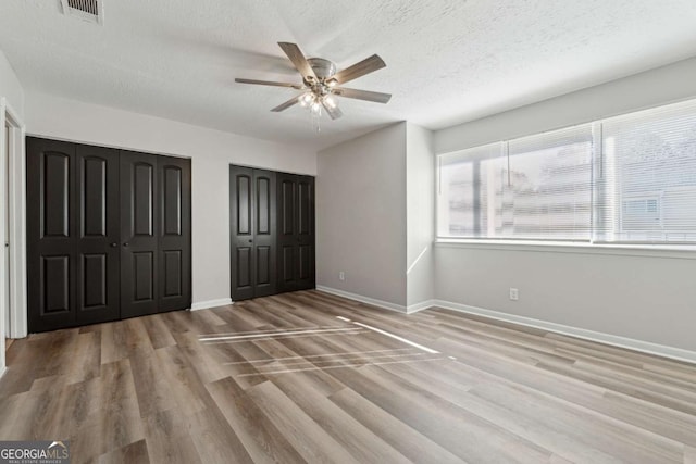 unfurnished bedroom with a textured ceiling, ceiling fan, two closets, and light hardwood / wood-style floors