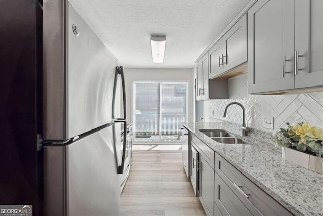 kitchen featuring light hardwood / wood-style flooring, sink, light stone counters, stainless steel appliances, and gray cabinets