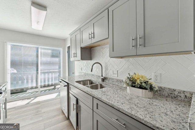 kitchen featuring sink, light hardwood / wood-style floors, stainless steel dishwasher, light stone countertops, and decorative backsplash