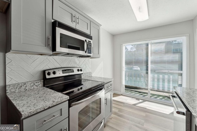 kitchen with appliances with stainless steel finishes, gray cabinets, and light stone countertops