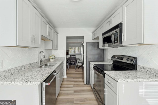 kitchen with appliances with stainless steel finishes, light stone countertops, light hardwood / wood-style floors, backsplash, and sink